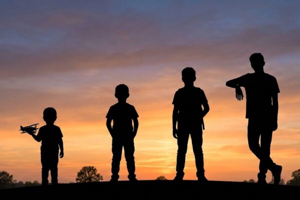 A sequence of four dark silhouettes of a child growing into an adolescent against a warm sunset sky.